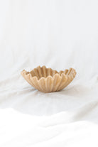 beige ruffle ceramic decorative bowl sitting against a white linen backdrop. 