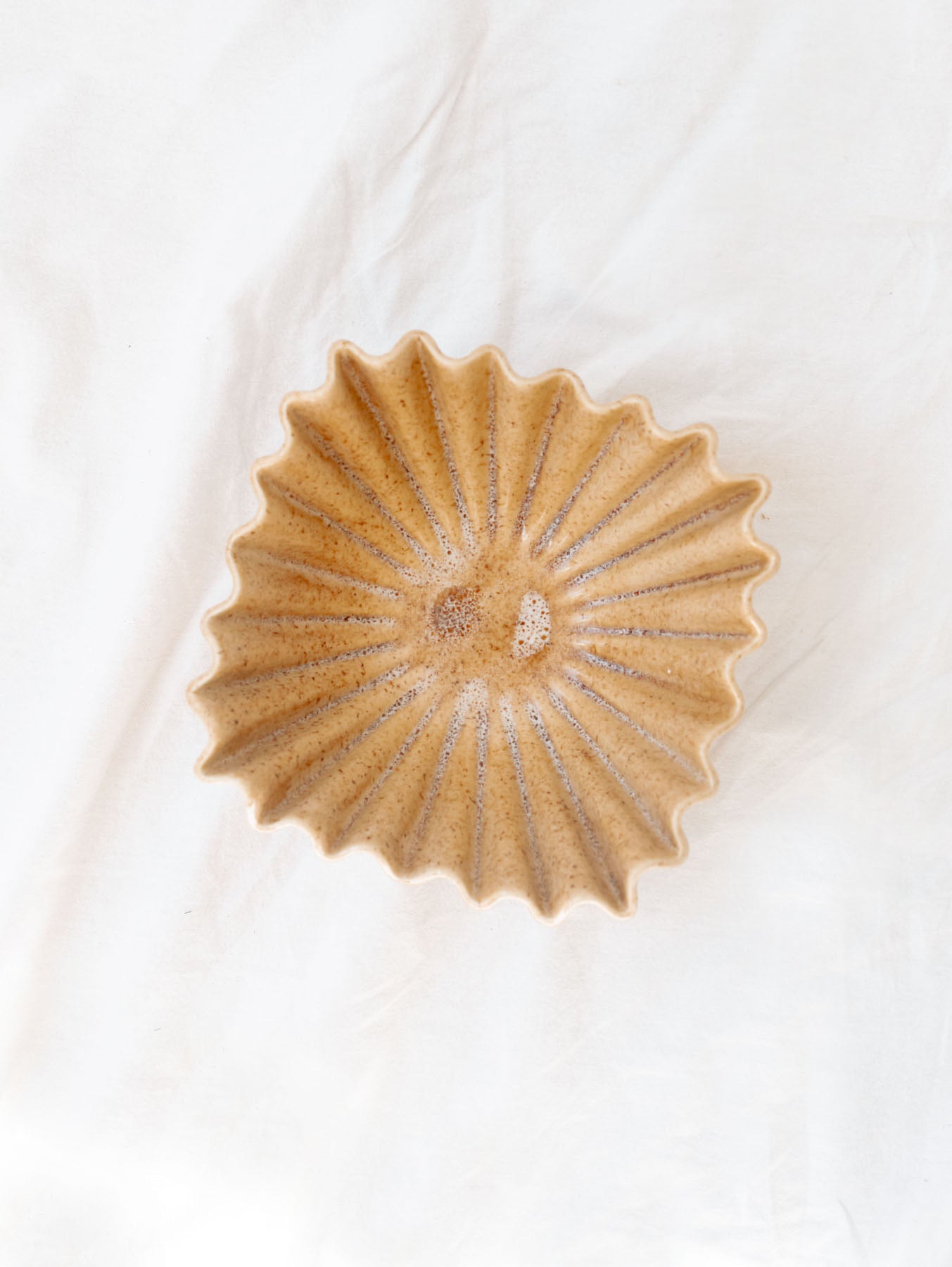 beige ruffle ceramic decorative bowl sitting against a white linen backdrop. 