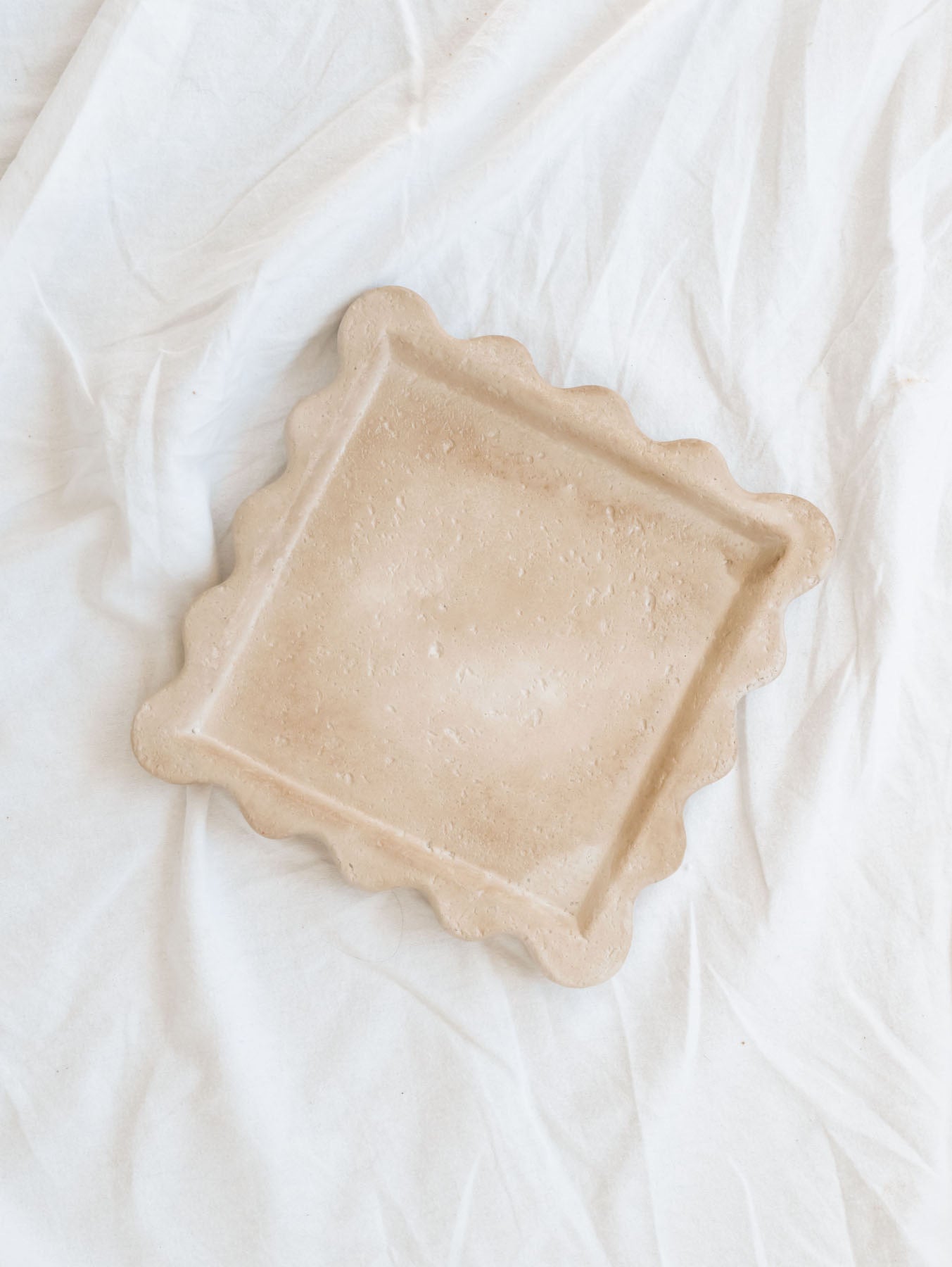 Top view of the 7.7" square cement scallop edge tray sitting on a white linen backdrop. 