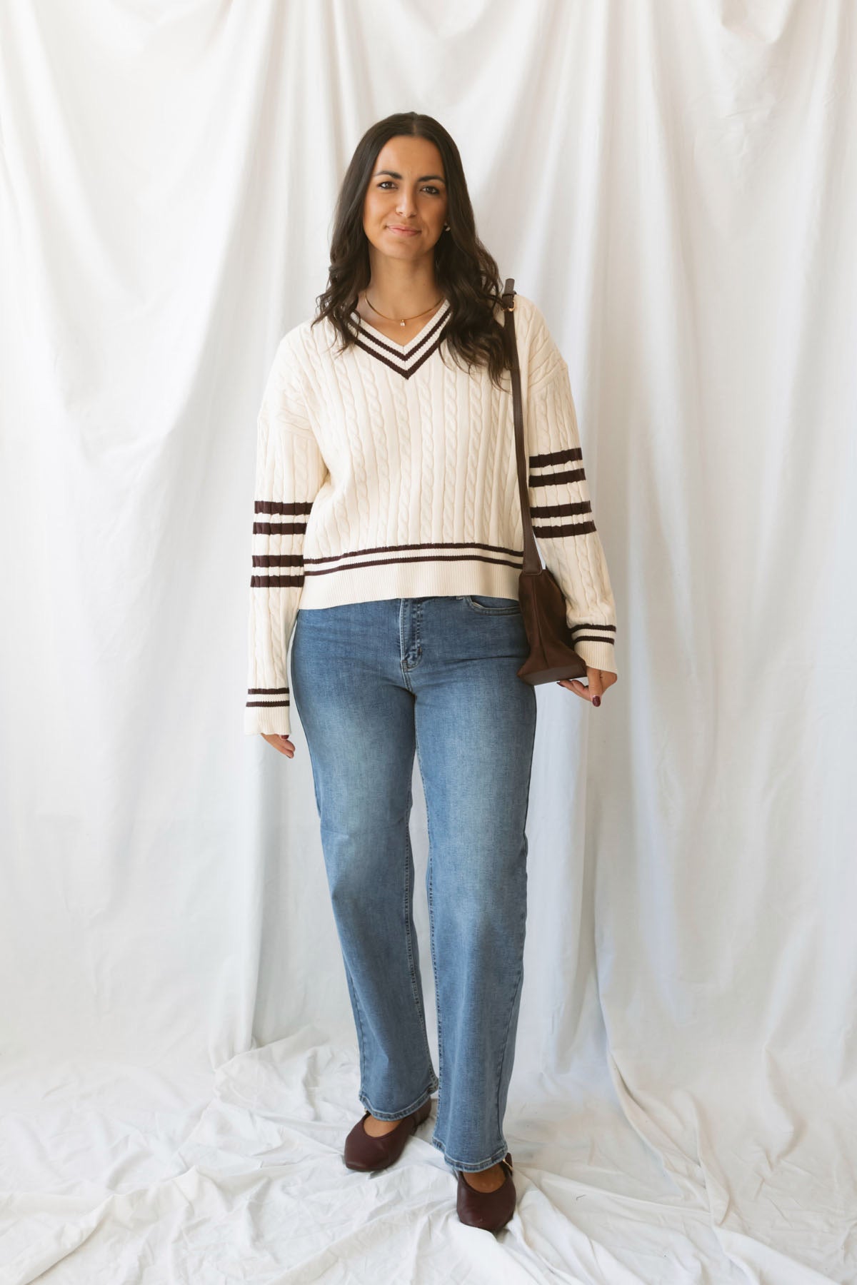 Charlotte cream cable knit V-neck varsity sweater with chocolate brown accents and classic collegiate-inspired details.