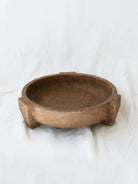 Side view of the footed cement bowl sitting on a white linen backdrop. 