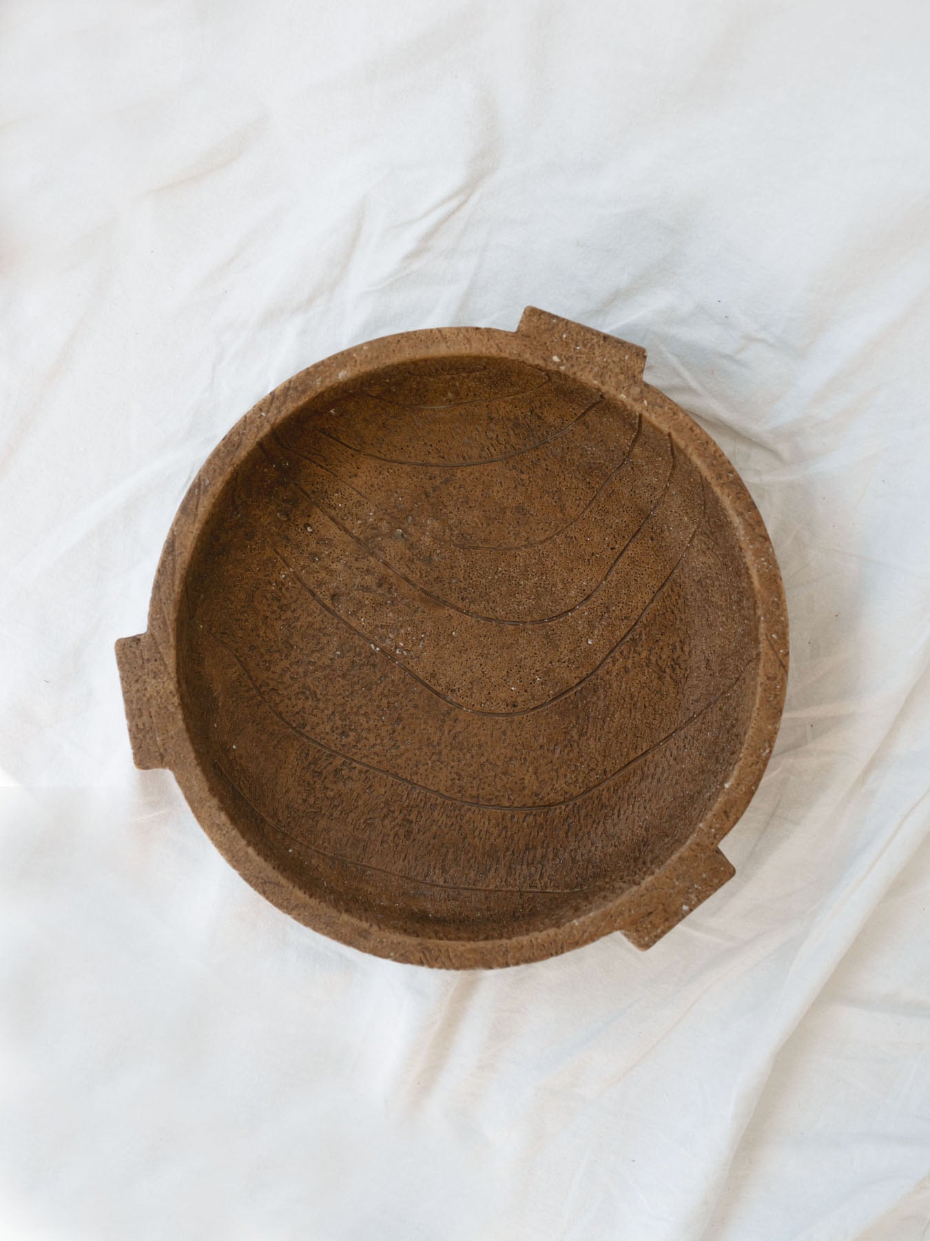 Top view of the footed cement bowl sitting on a white linen backdrop. 