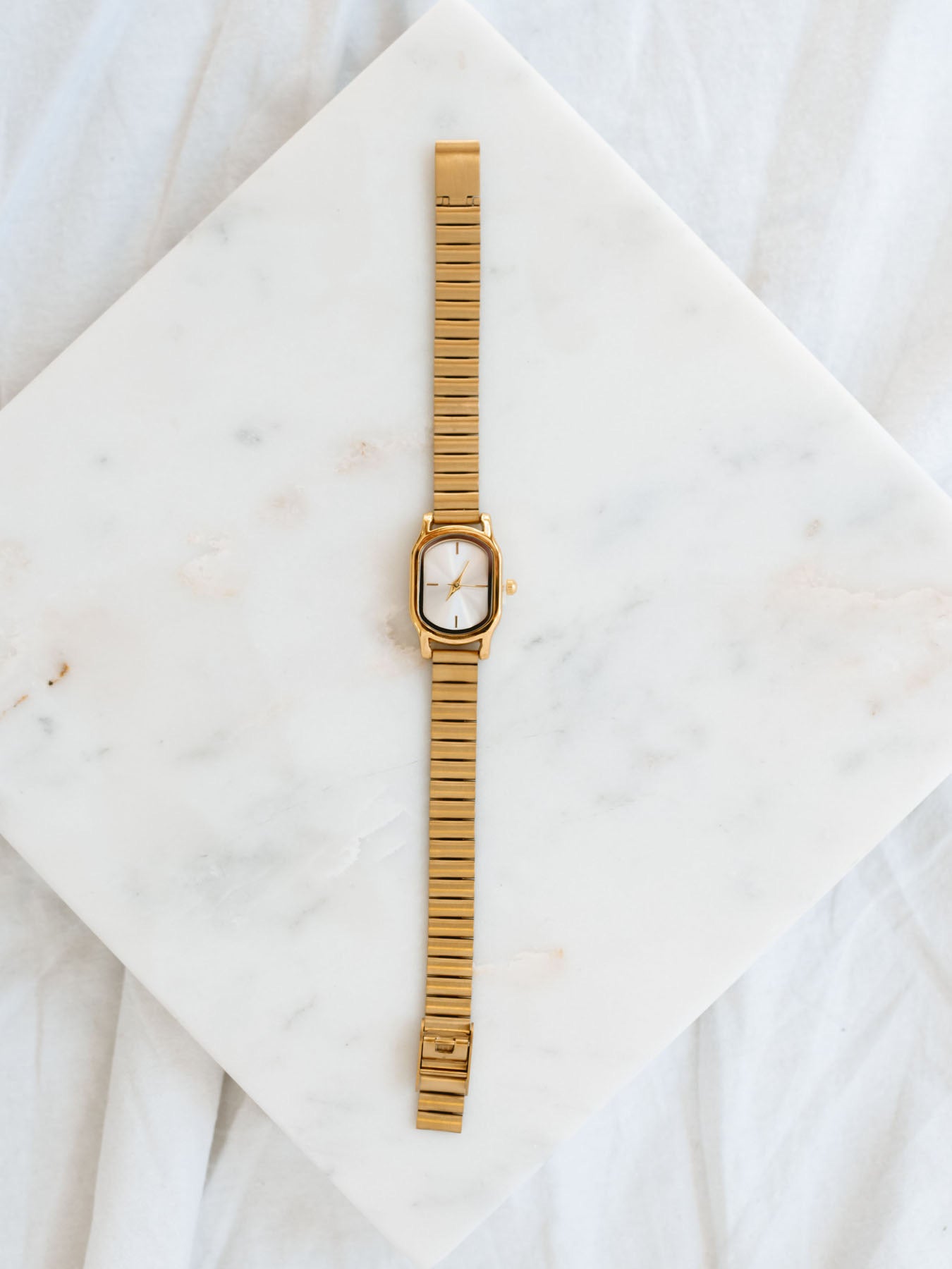 Gold watch with oval face laying out on marble board. 