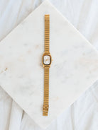 Gold watch with oval face laying out on marble board. 