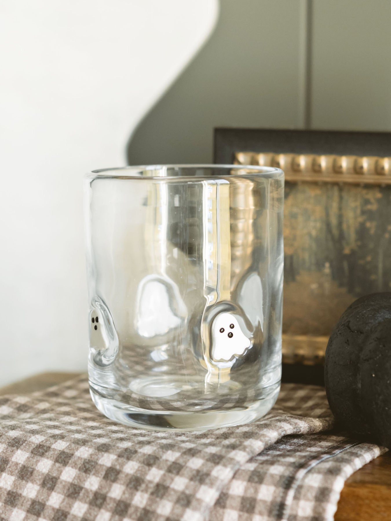 Showing the drinking glass with embedded ghosts sitting on a warm wood board with a checkered geometry towel layered under the glass. 