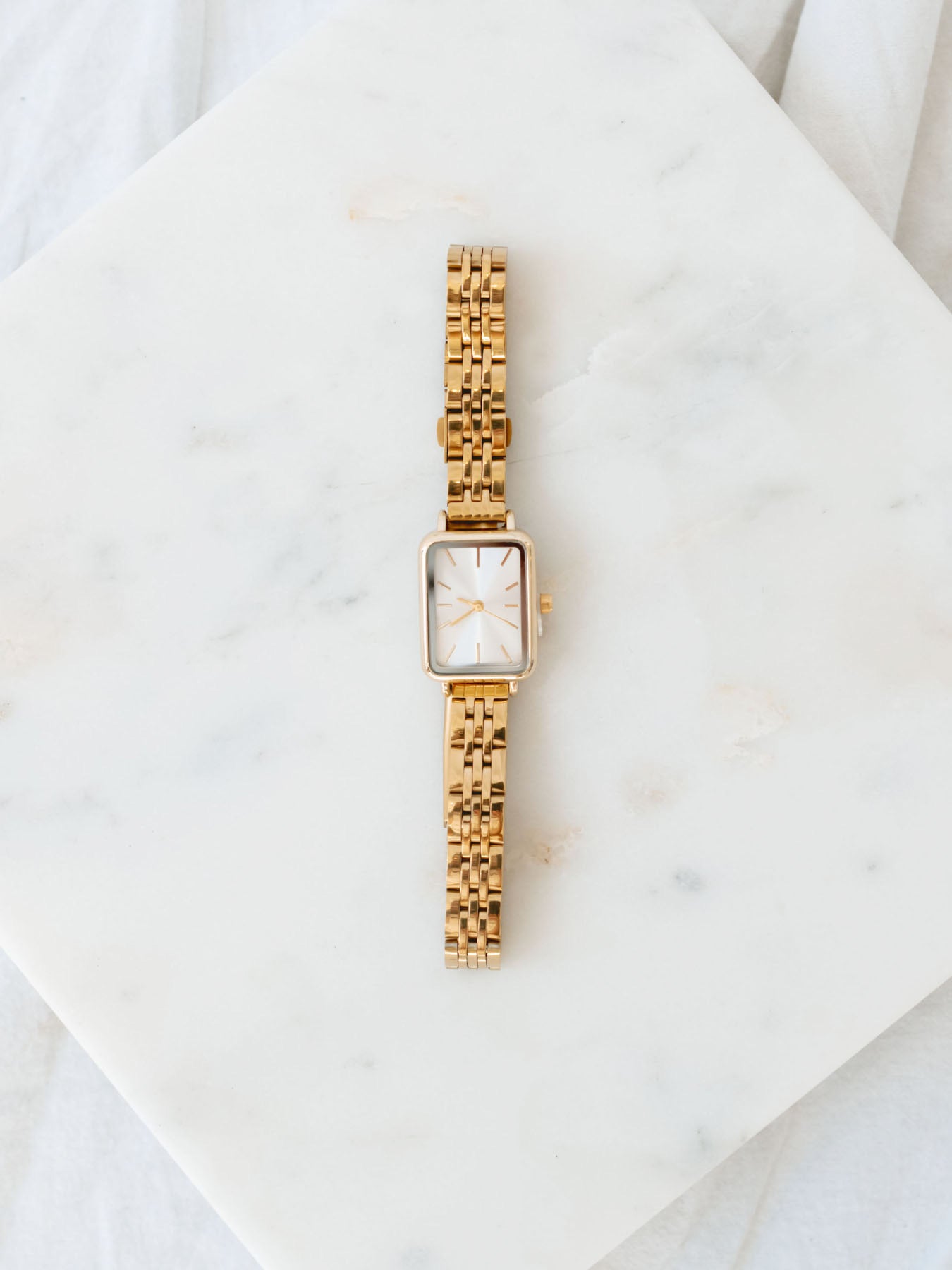 Gold watch with rectangle face laying on marble board. 
