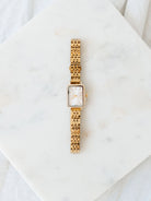 Gold watch with rectangle face laying on marble board. 