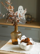 Amber glass vase filled with a brown eucalyptus layered with the white ghost bowl and a beige placemat. 