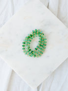 Green and gold beaded bracelet stack laying on a marble board.