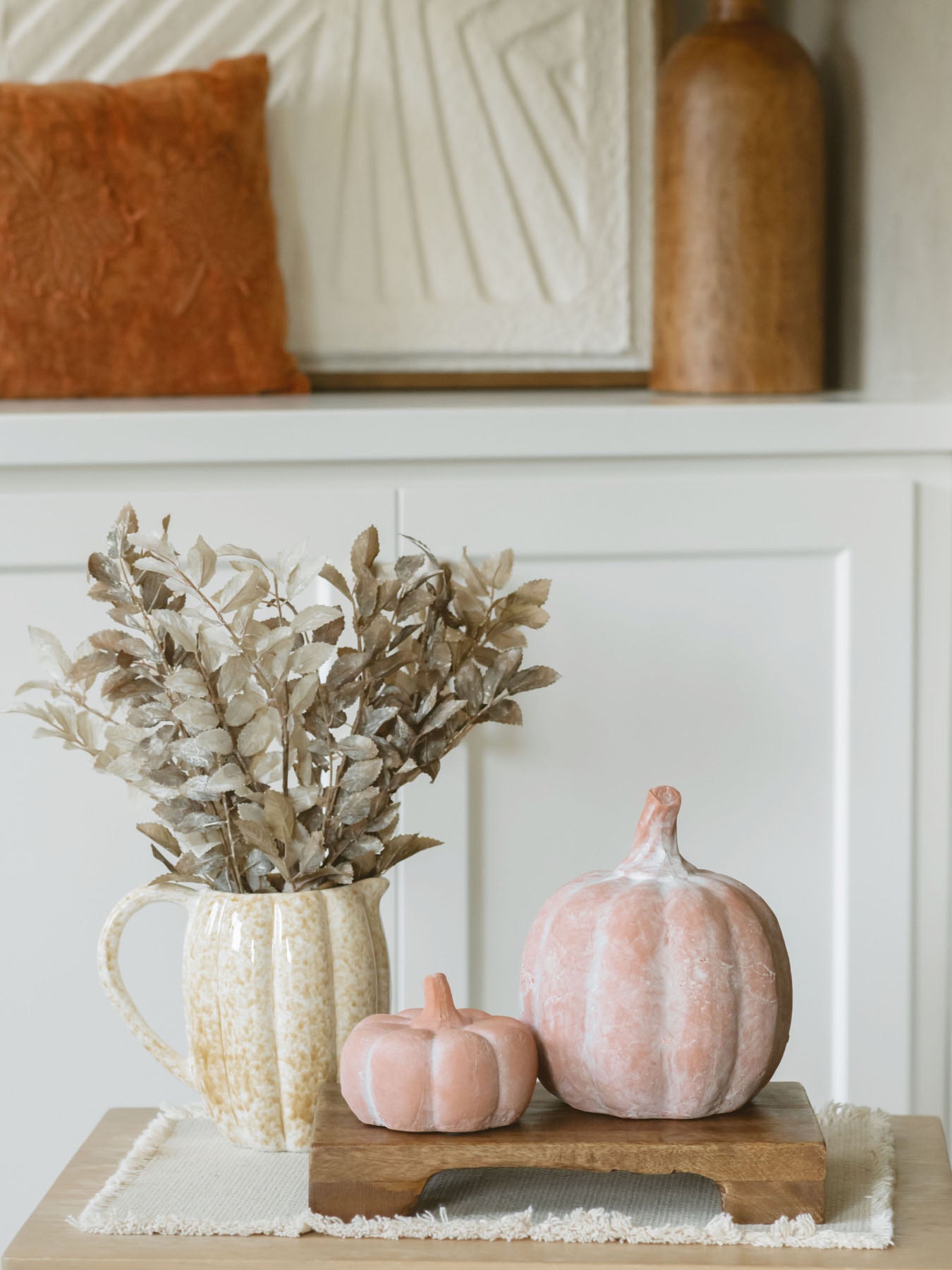 Orange terracotta pumpkins sitting next to each other on a warm wood riser with a pumpkin shaped pitcher and fall foilage. 