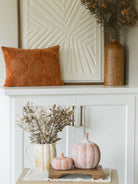 Burnt orange leaf pillow layered on cabinet with large textured art piece and wood vase with sprig. 