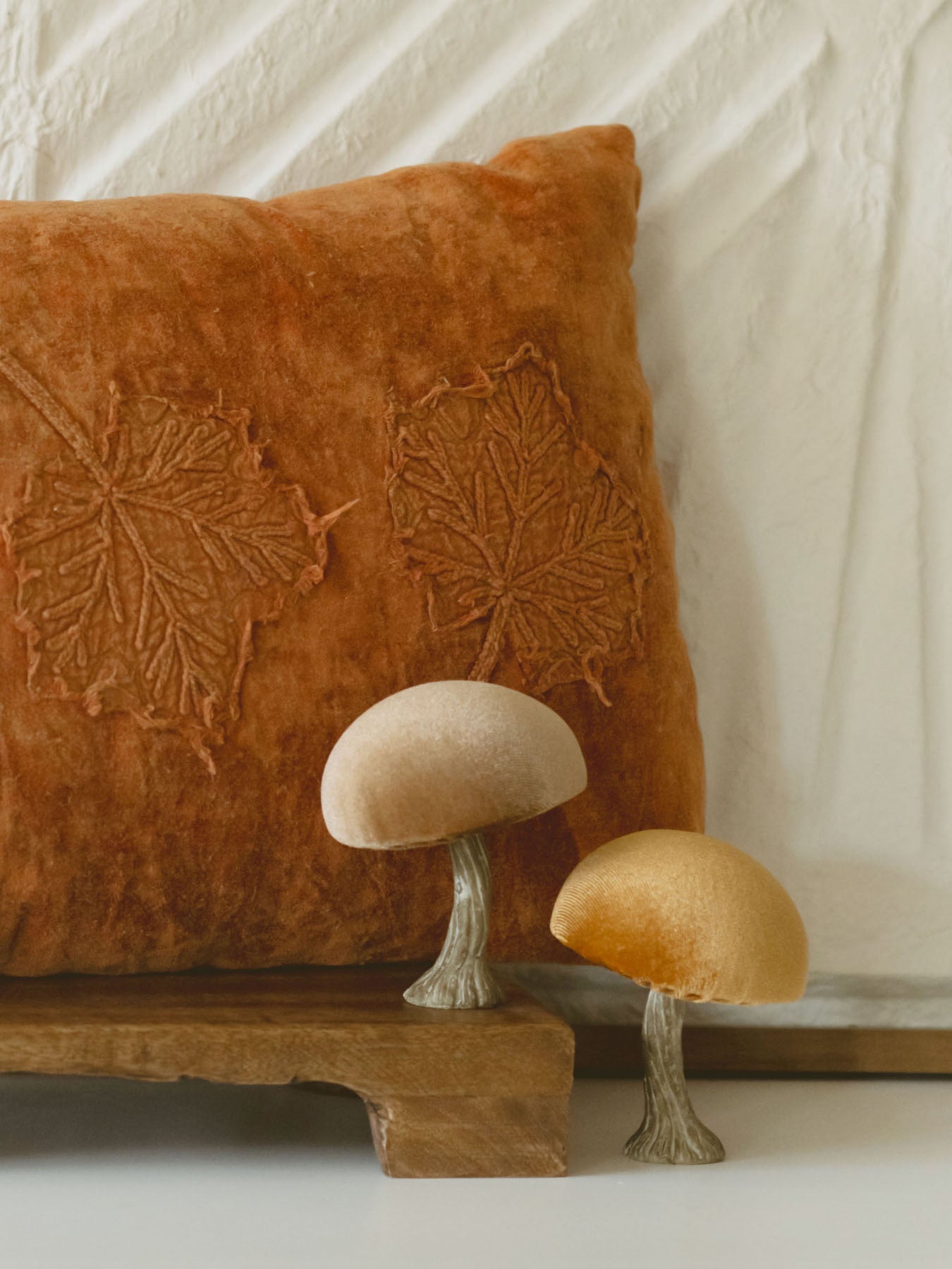 The champagne and mustard mushroom paired together with a rusty orange pillow set on a warm wood board. 
