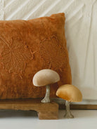 Burnt orange leaf pillow layered on cabinet with two whimsical velvet mushrooms. 