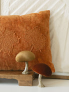 The champagne and rust mushroom paired together with a rusty orange pillow set on a warm wood board. 