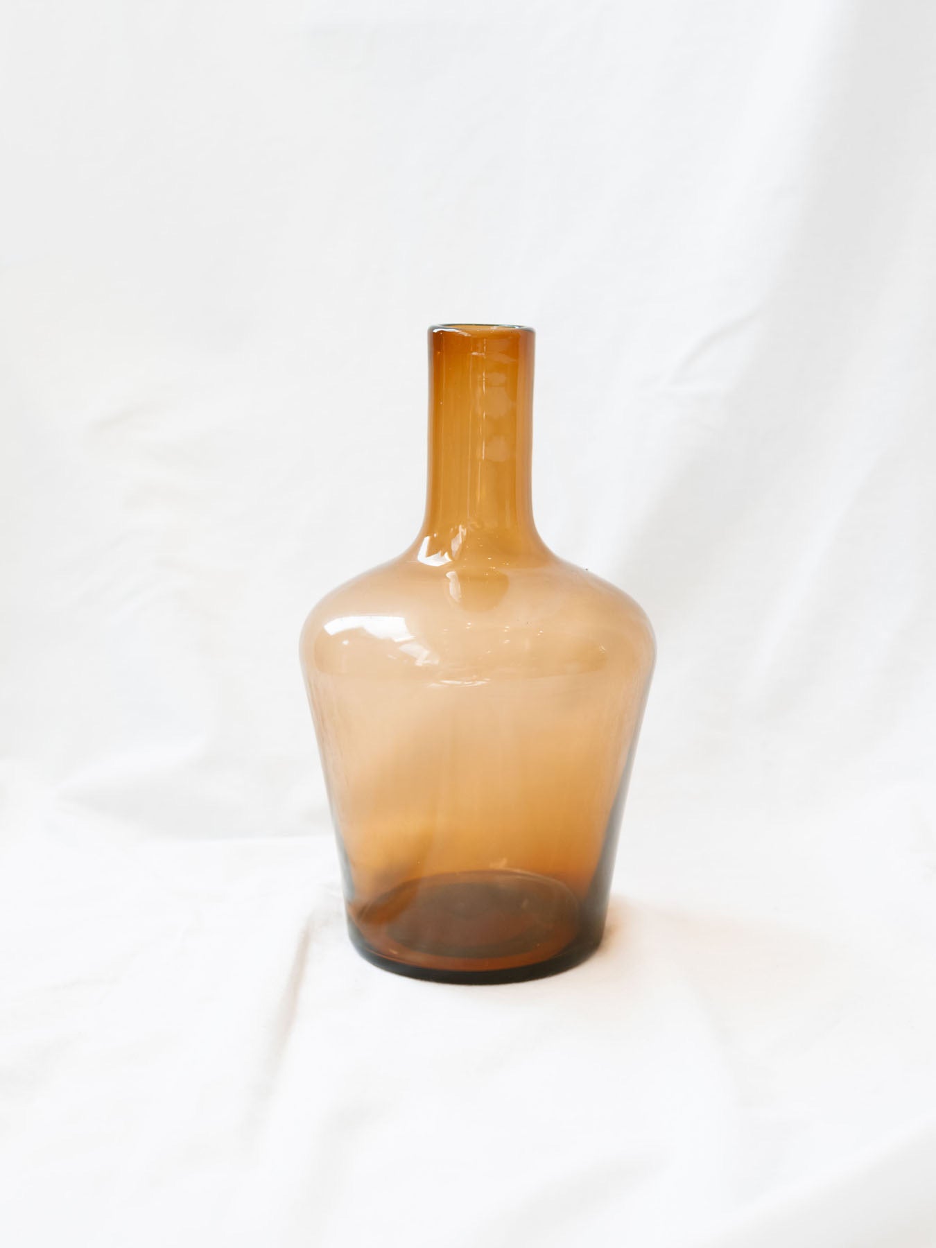 Amber glass vase sitting on white linen backdrop. 
