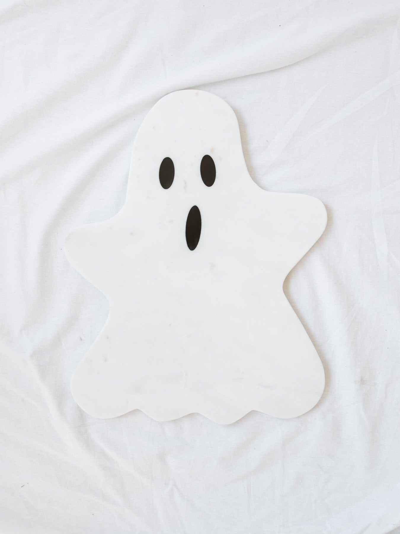 Marble ghost board in white with black details laying on white linen backdrop. 