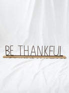 Be Thankful style metal and wood sign sitting on white linen backdrop.