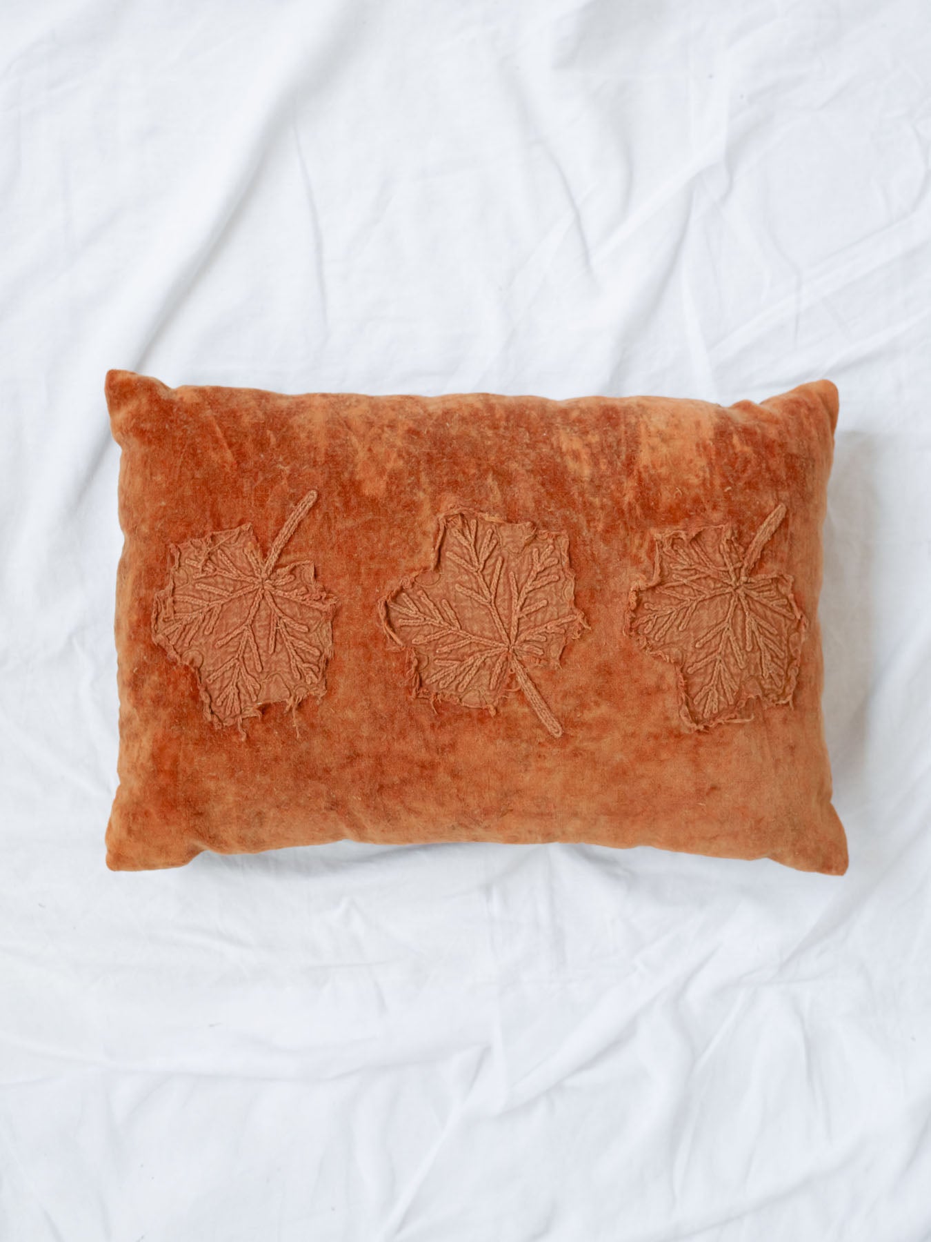 Velvet rectangle pillow with leaf print laying on white linen backdrop. 