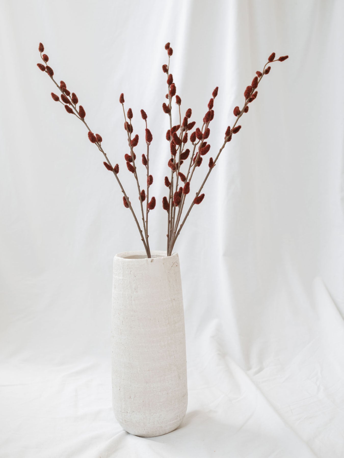 Florist stem sitting in tall white vase on white linen backdrop.