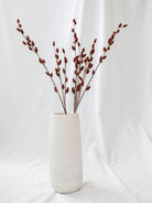 Florist stem sitting in tall white vase on white linen backdrop.
