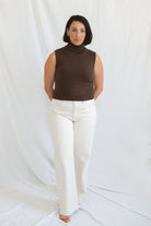 Model wearing the brown sleeveless knit turtleneck. Styled with a cream highwaist denim pant. 