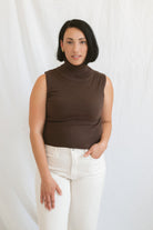 Model wearing the brown sleeveless knit turtleneck. Styled with a cream highwaist denim pant. 
