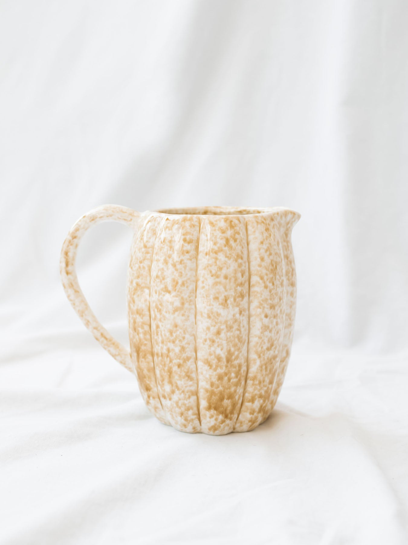 Showing the stoneware pitcher empty sitting on a white linen backdrop. 