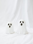 Two sizes of the white ceramic ghosts sitting next to each other on a white linen backdrop. 
