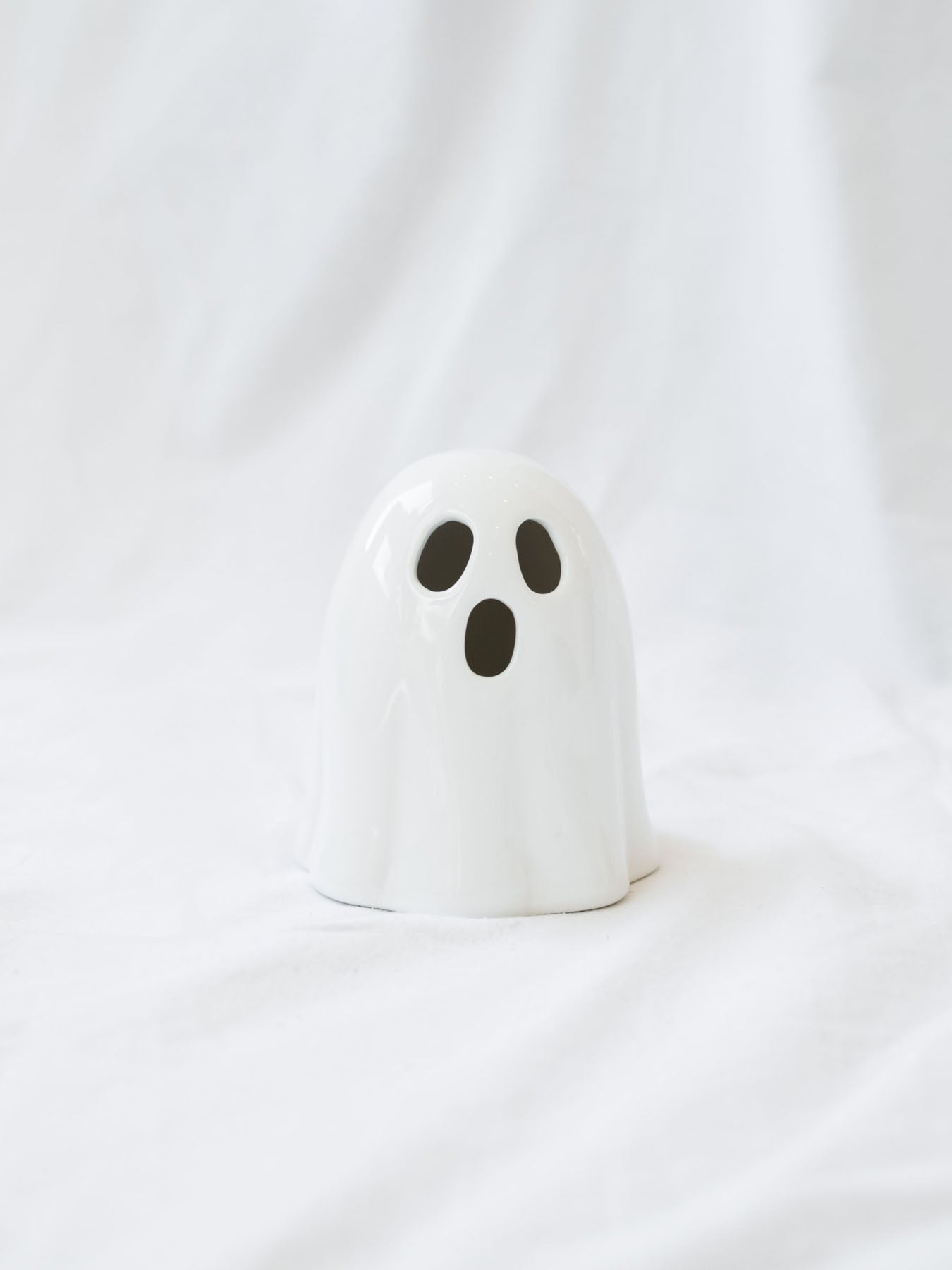 The smaller shorter style of the LED ceramic white ghost sitting on a white linen backdrop. 
