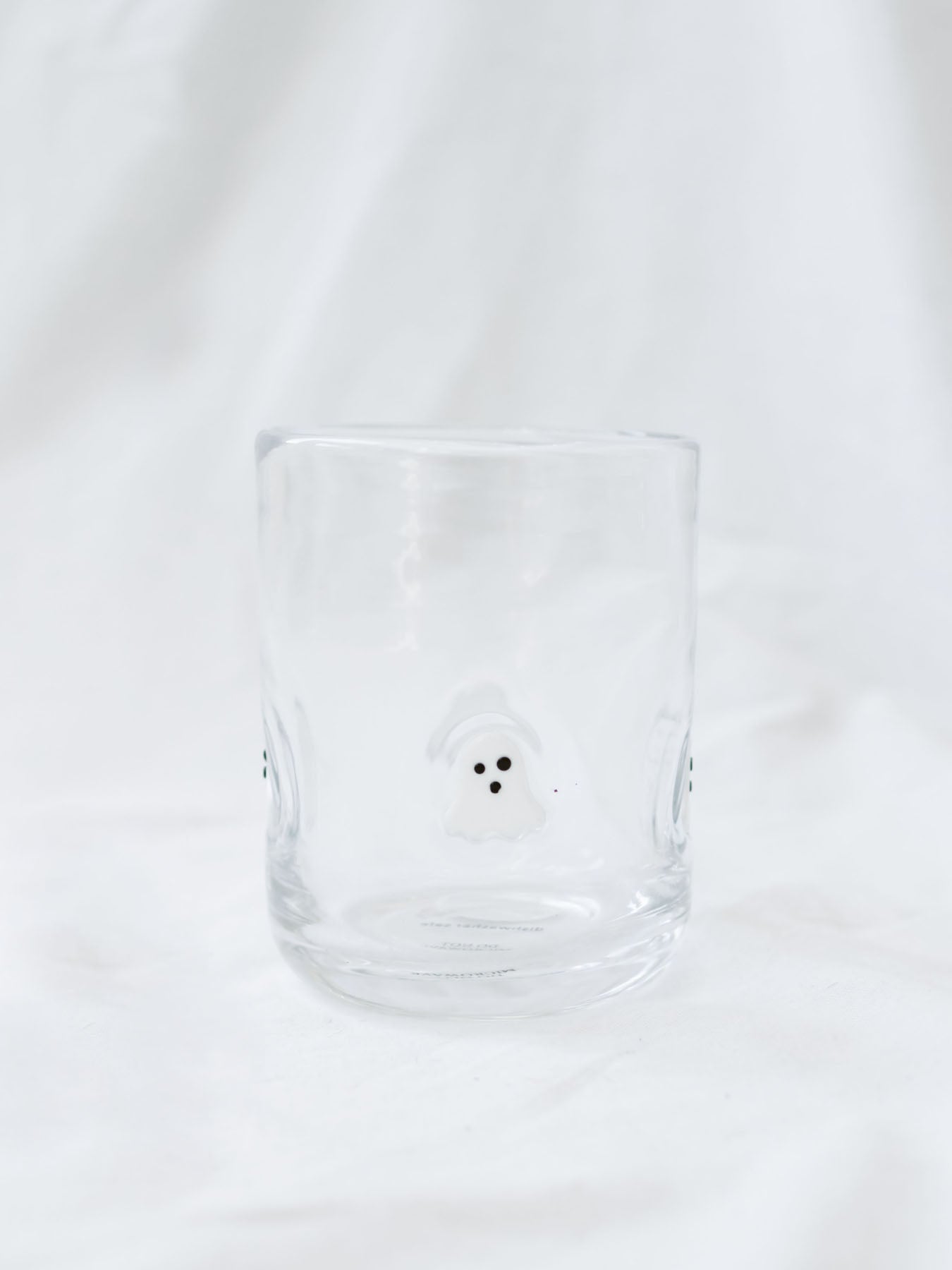 Showing the drinking glass with embedded ghosts sitting on a white linen backdrop. 