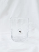 Showing the drinking glass with embedded ghosts sitting on a white linen backdrop. 