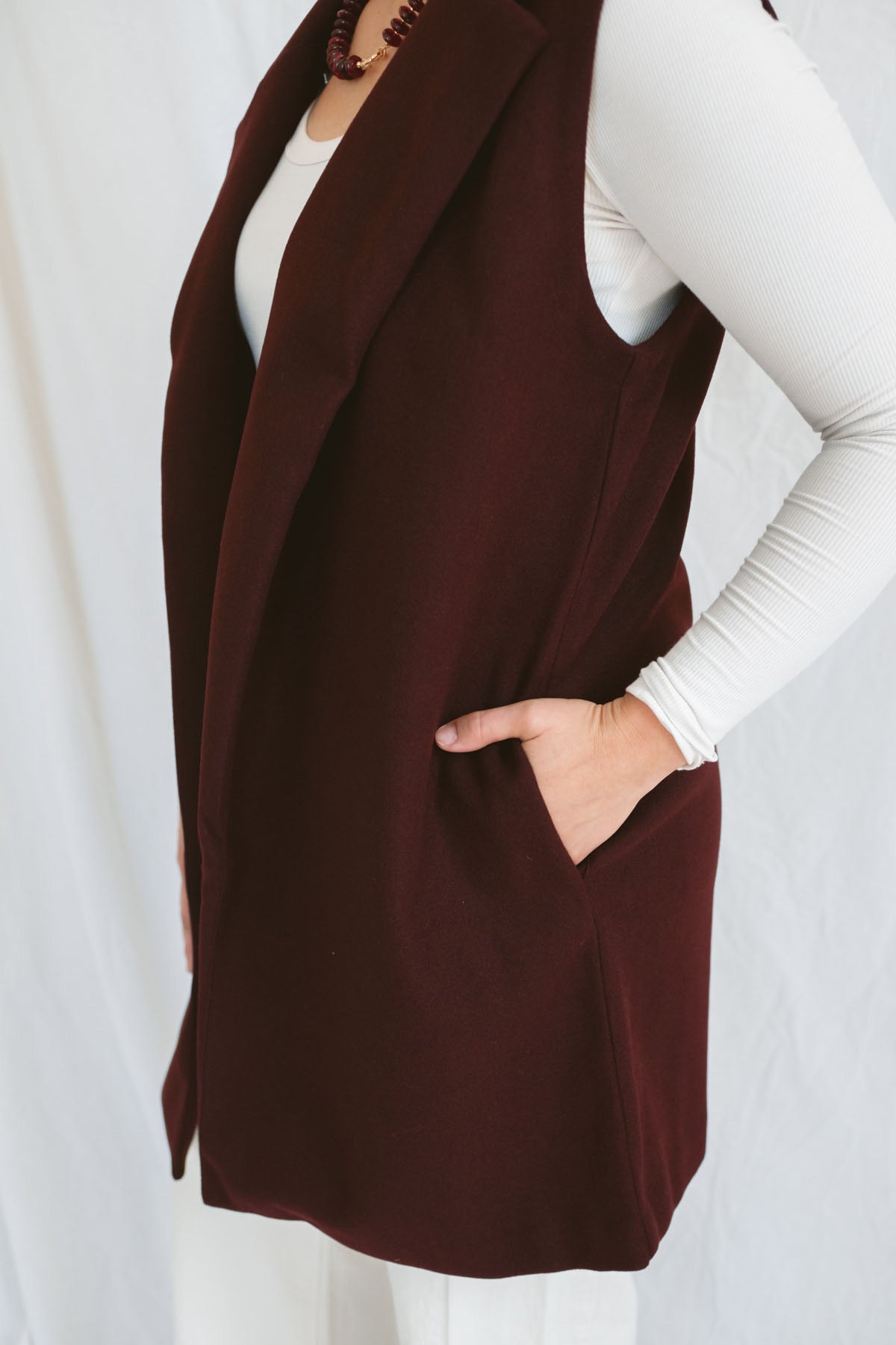 Model wearing the open sleeveless notched collar vest in burgundy color.