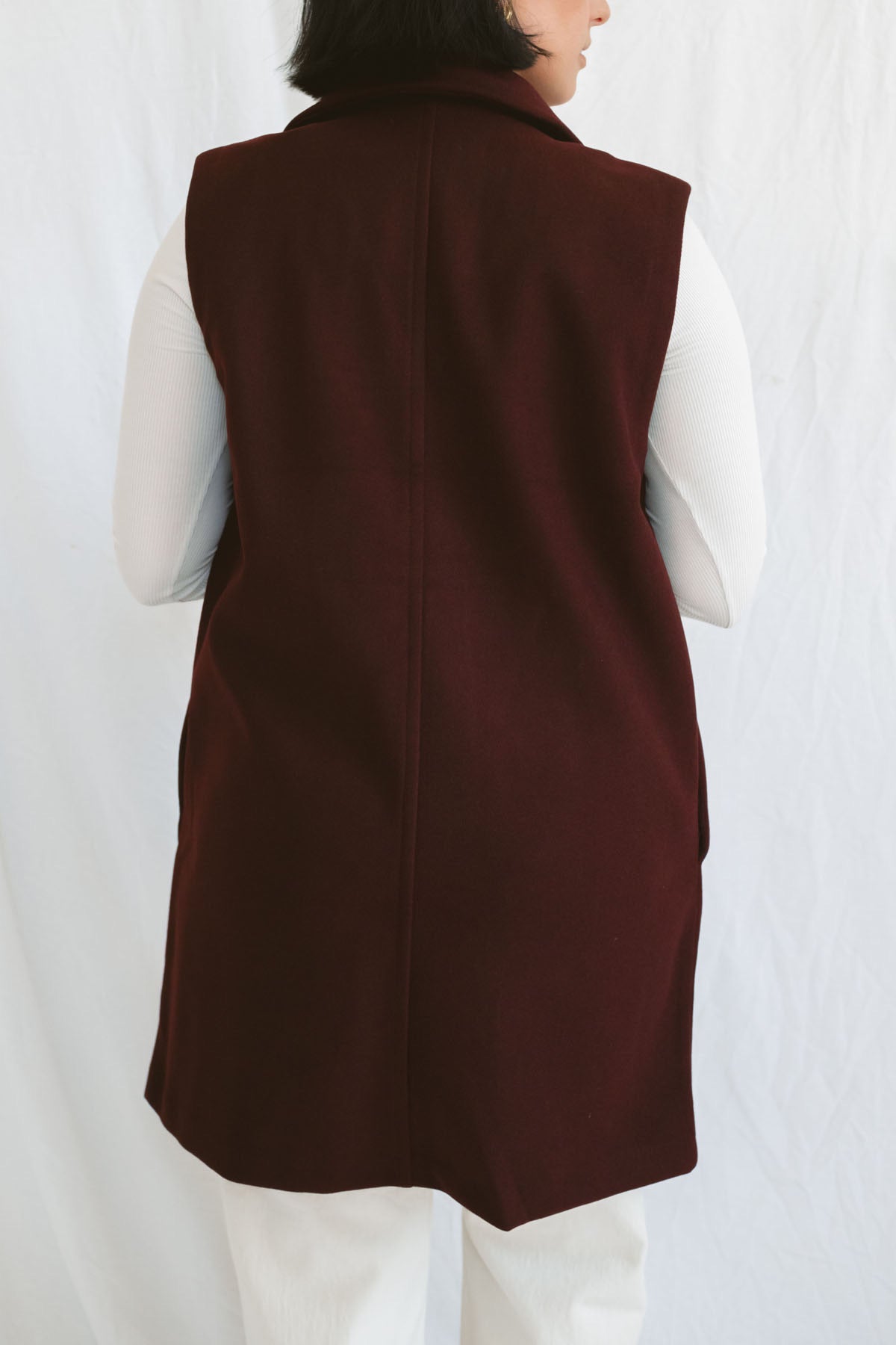 Model wearing the open sleeveless notched collar vest in burgundy color.