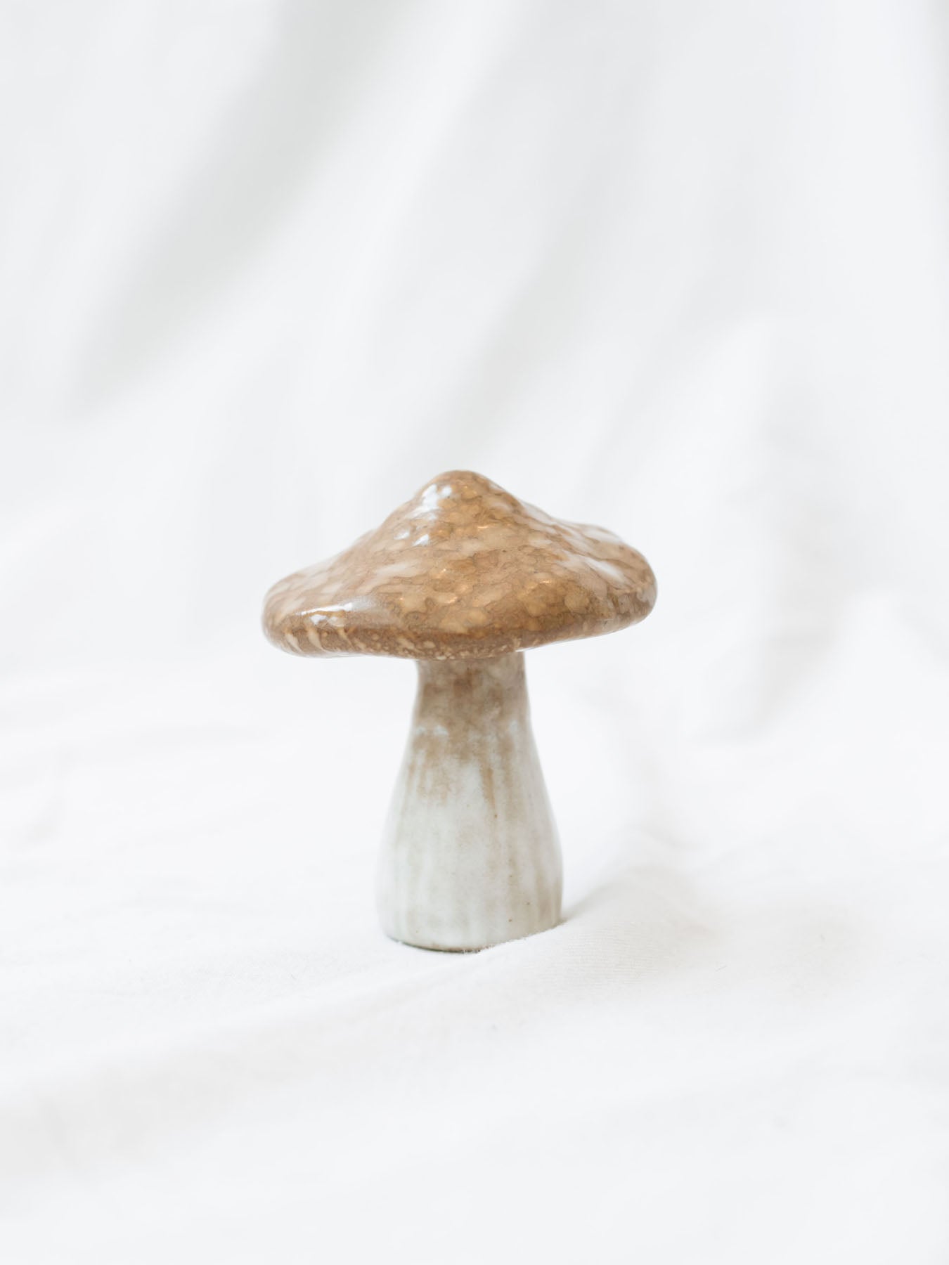 Close up of the small stoneware mushroom sitting on a white linen backdrop. 