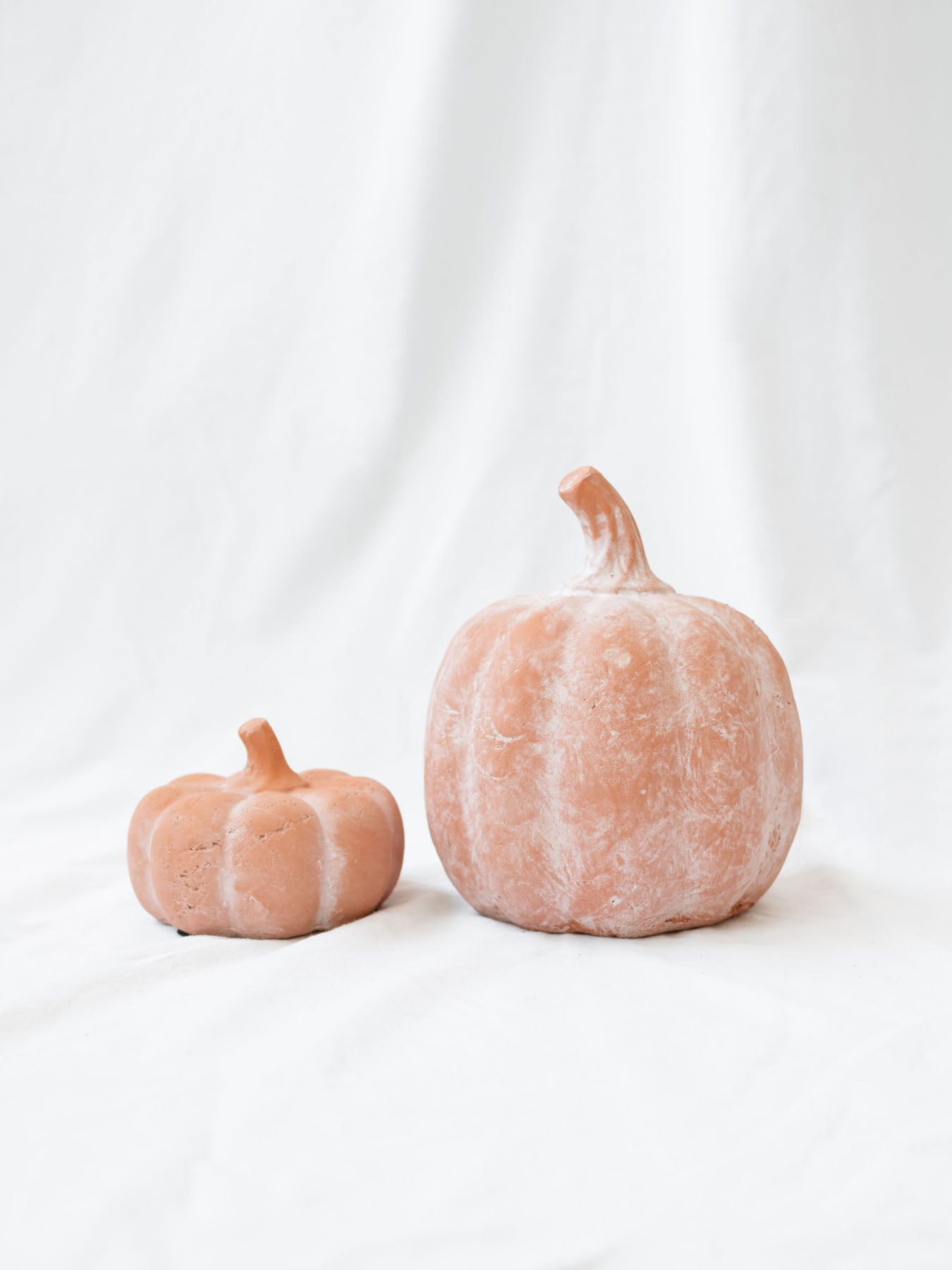 Orange terracotta pumpkins sitting next to each other on a white linen backdrop. 