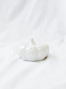 White ceramic textured pumpkin shown sitting on white linen backdrop. 