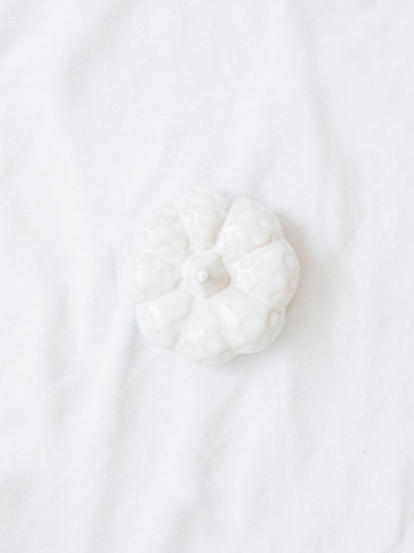 Top view of the white ceramic textured pumpkin shown sitting on white linen backdrop. 