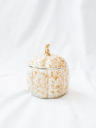 Stoneware pumpkin shaped jar with lid on top sitting on white linen backdrop.