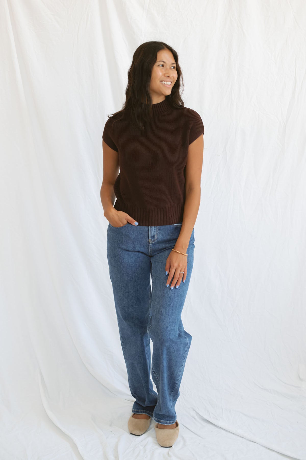 Model wearing mock neck extended shoulder top in brown. 