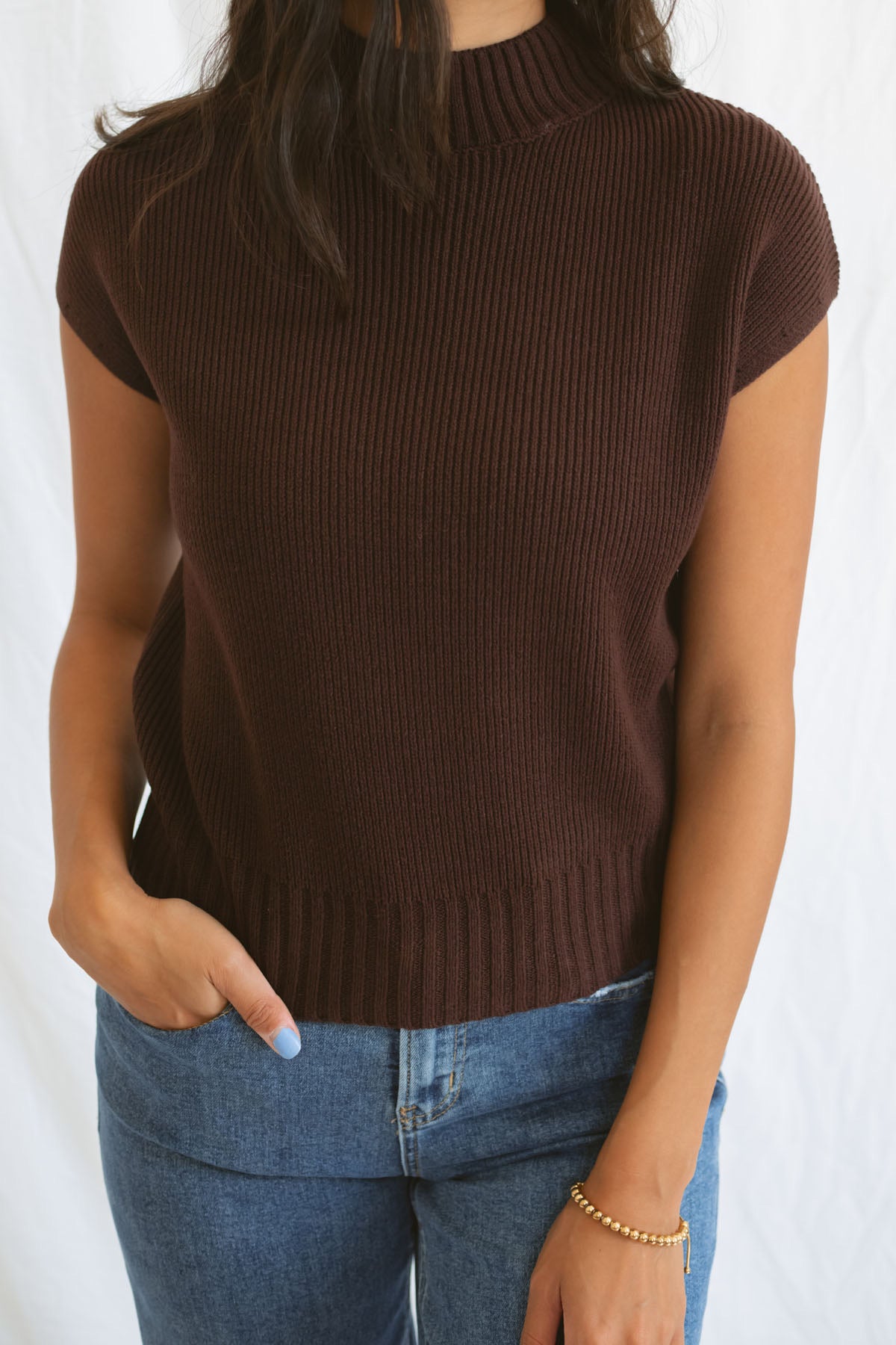 Model wearing mock neck extended shoulder top in brown. 