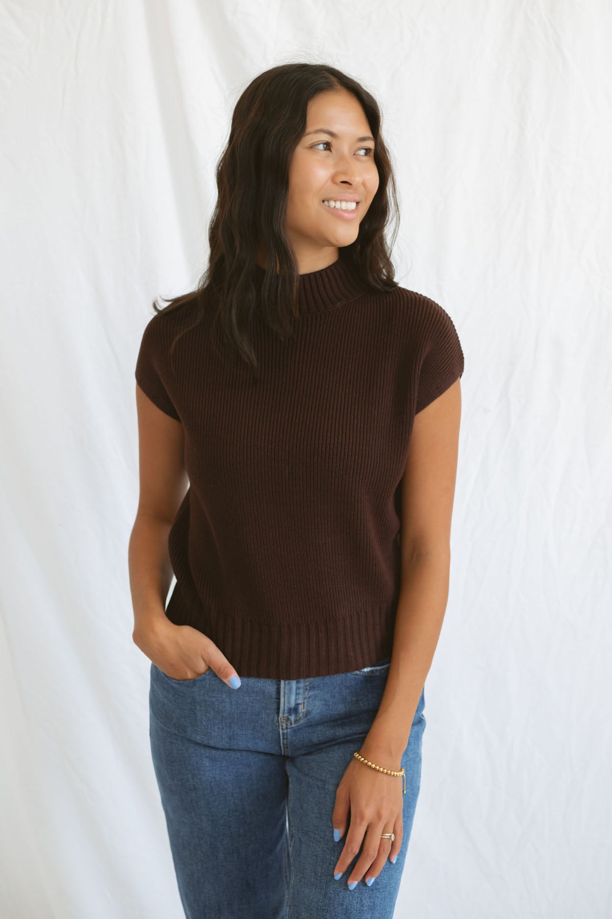 Model wearing mock neck extended shoulder top in brown. 
