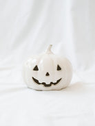 The Small shorter size of the white ceramic jack-o-lanterns sitting on a white linen backdrop. 