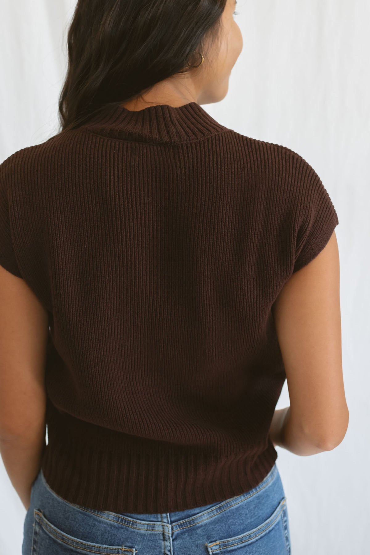Model wearing mock neck extended shoulder top in brown. 