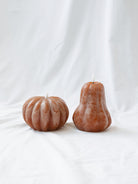 The pumpkin & gourd shape LED candle sitting next to each other on a white linen backdrop. 