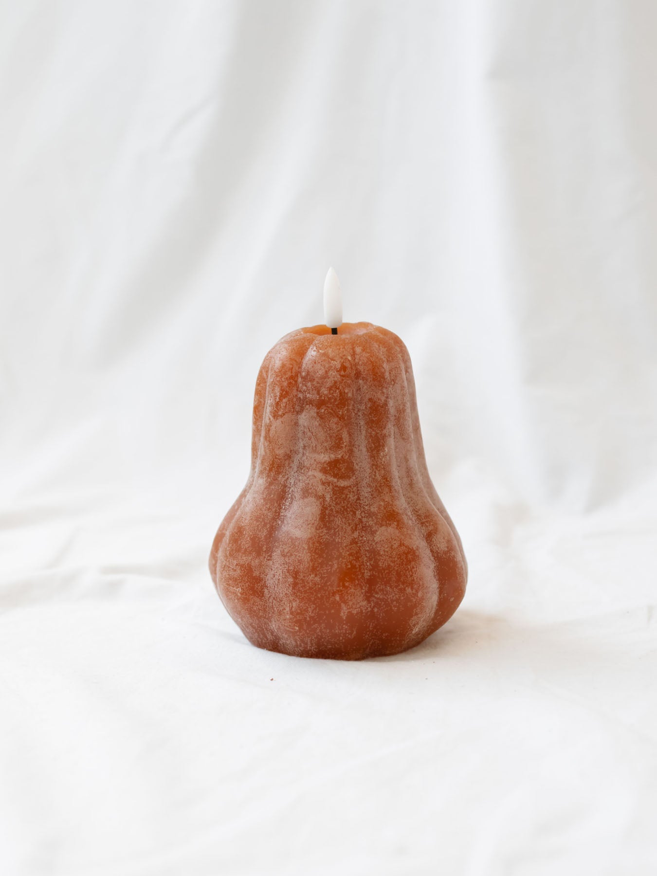 The gourd shaped LED candle sitting on a white linen backdrop. 