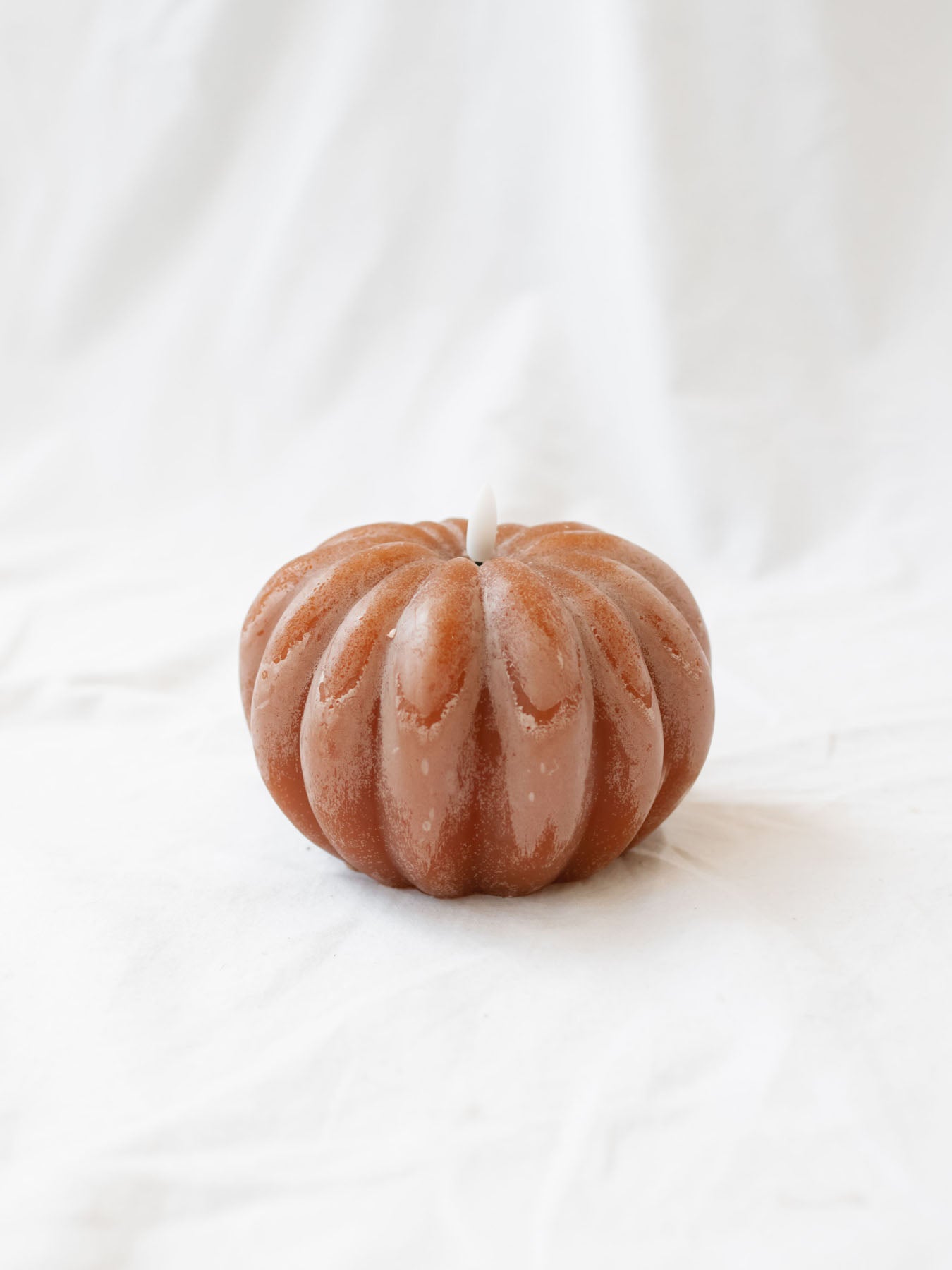 The Pumpkin shaped LED candle sitting on a white linen backdrop. 