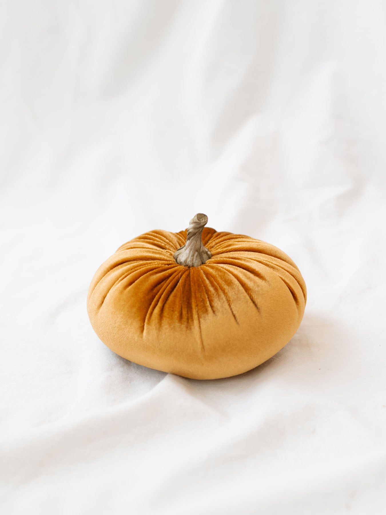 Orange color of the velvet pumpkins sitting on the white linen backdrop. 