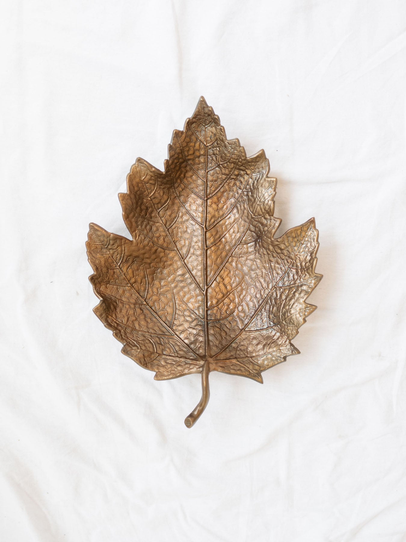 Antique gold leaf dish laying empty on a white linen backdrop.