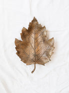 Antique gold leaf dish laying empty on a white linen backdrop.