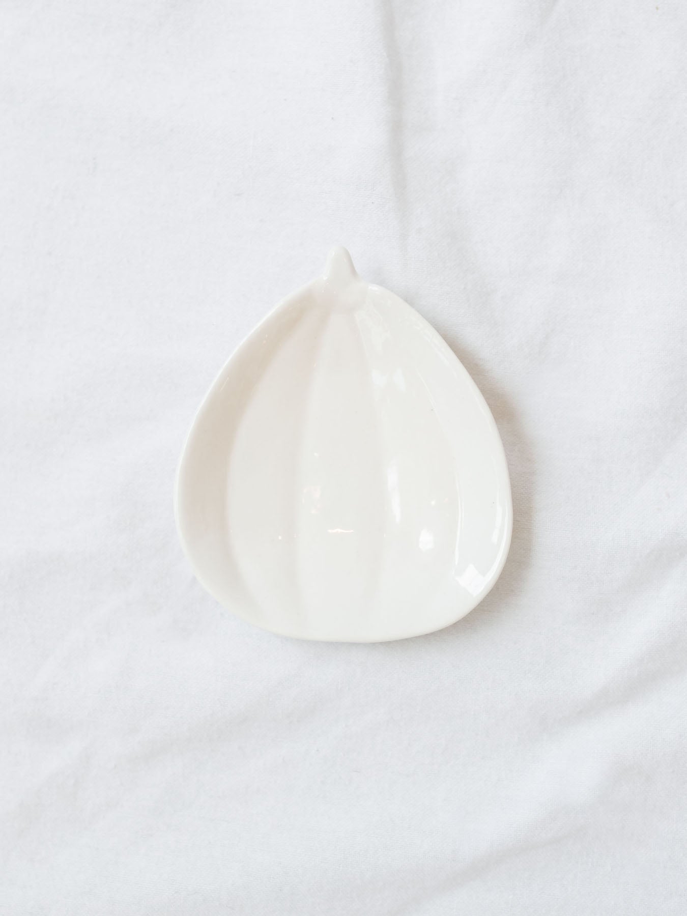 Mini stoneware pumpkin dish in white sitting on a white linen backdrop. 